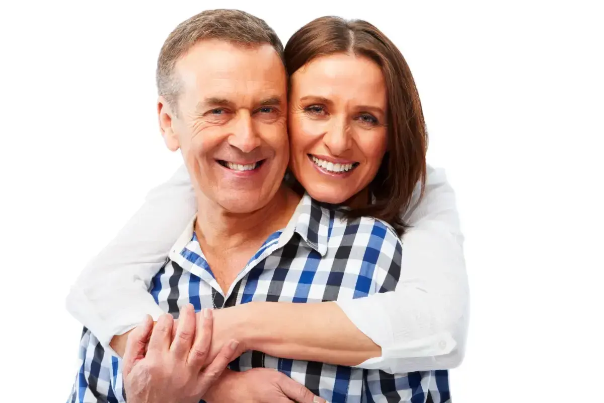 Smiling middle-aged couple embracing, showcasing healthy teeth and denture benefits.
