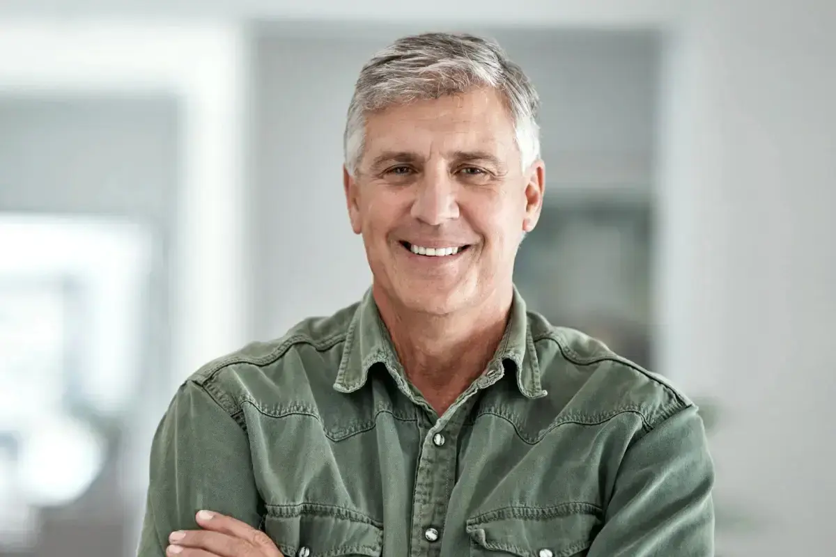 Middle-aged man smiling in dental office setting wearing olive shirt.