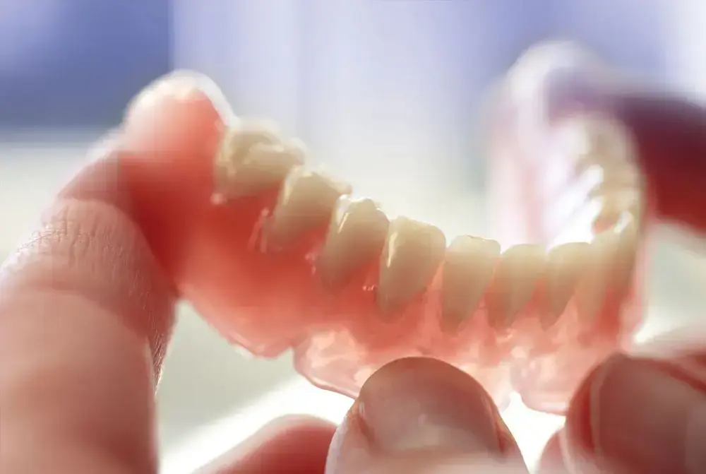 Close-up of a partial denture held in hands, showing artificial teeth against pink gum base.