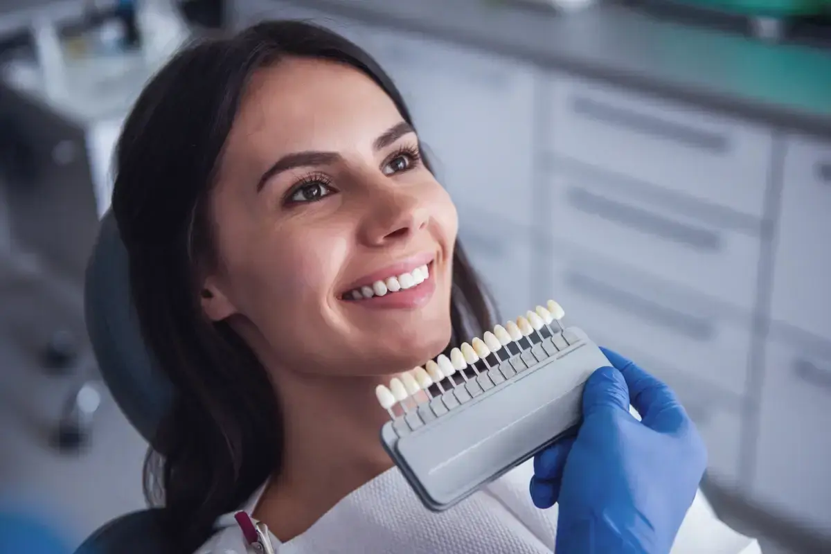 Woman smiling while holding a dental veneer shade guide for tooth color selection.