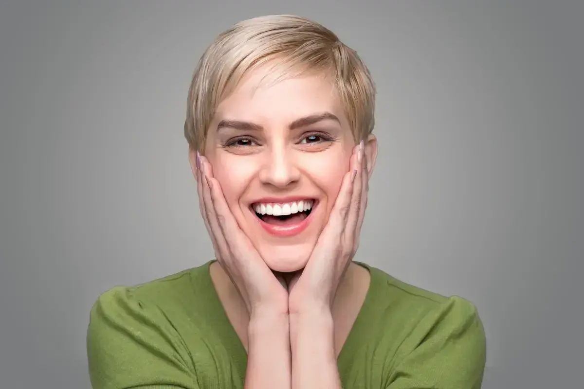 Woman smiling with hands to face showcasing bright teeth and cosmetic dental results.