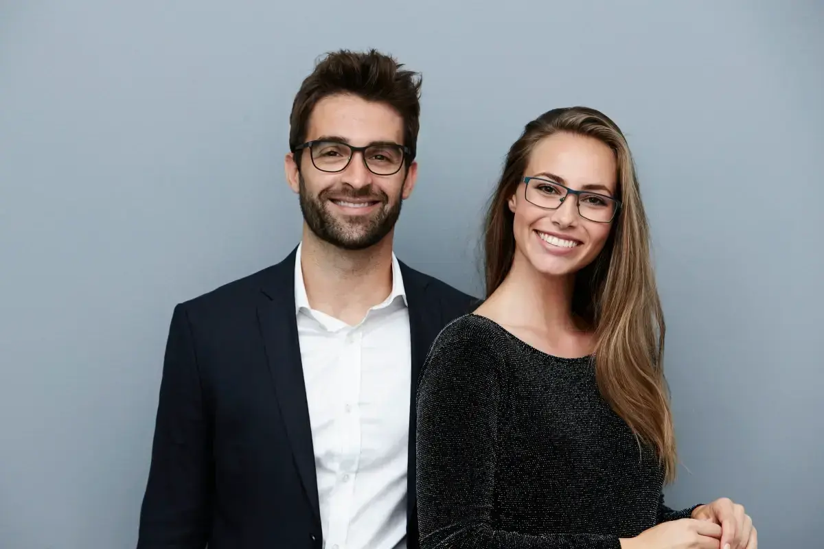 Two smiling professionals wearing glasses in a dental practice portrait.